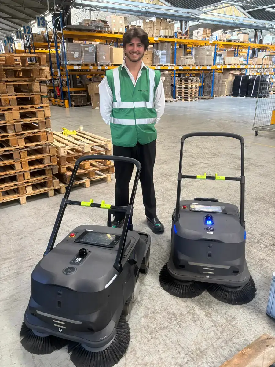 Un membre de l'équipe Elio Robot avec deux robots balayeurs autonomes chez un client