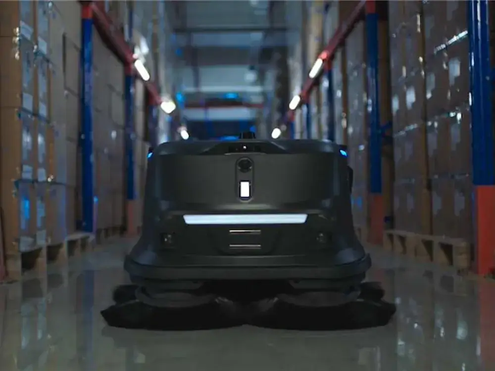 Robot de nettoyage industriel Pudu MT1 Vac balayant une allée entre deux racks de stockage