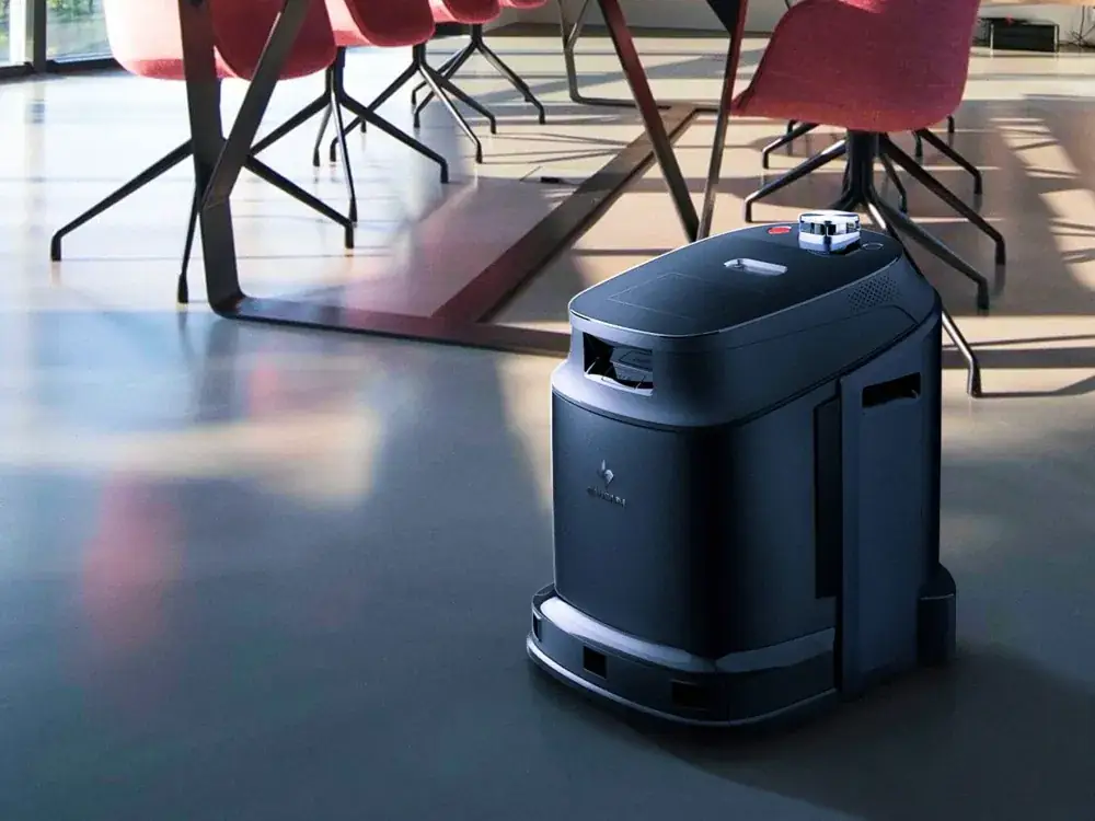 Robot de nettoyage autonome compact lavant le sol d'une salle, entre tables et chaises