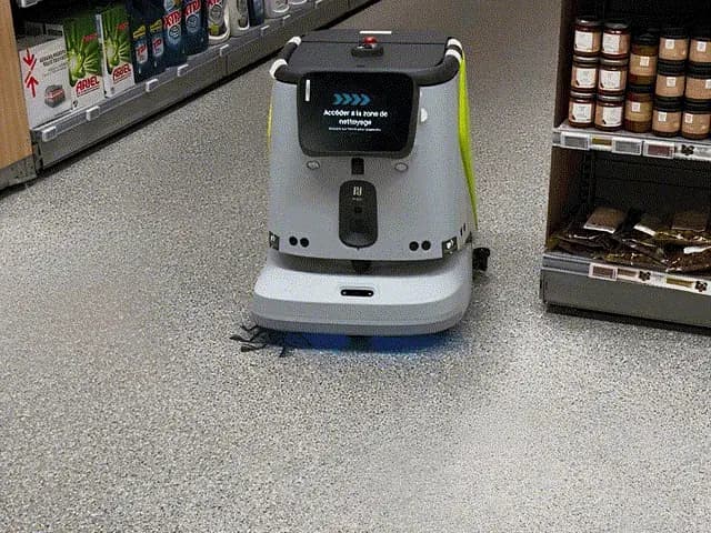 Robot de nettoyage autonome accédant à sa zone de nettoyage dans une allée de supermarché